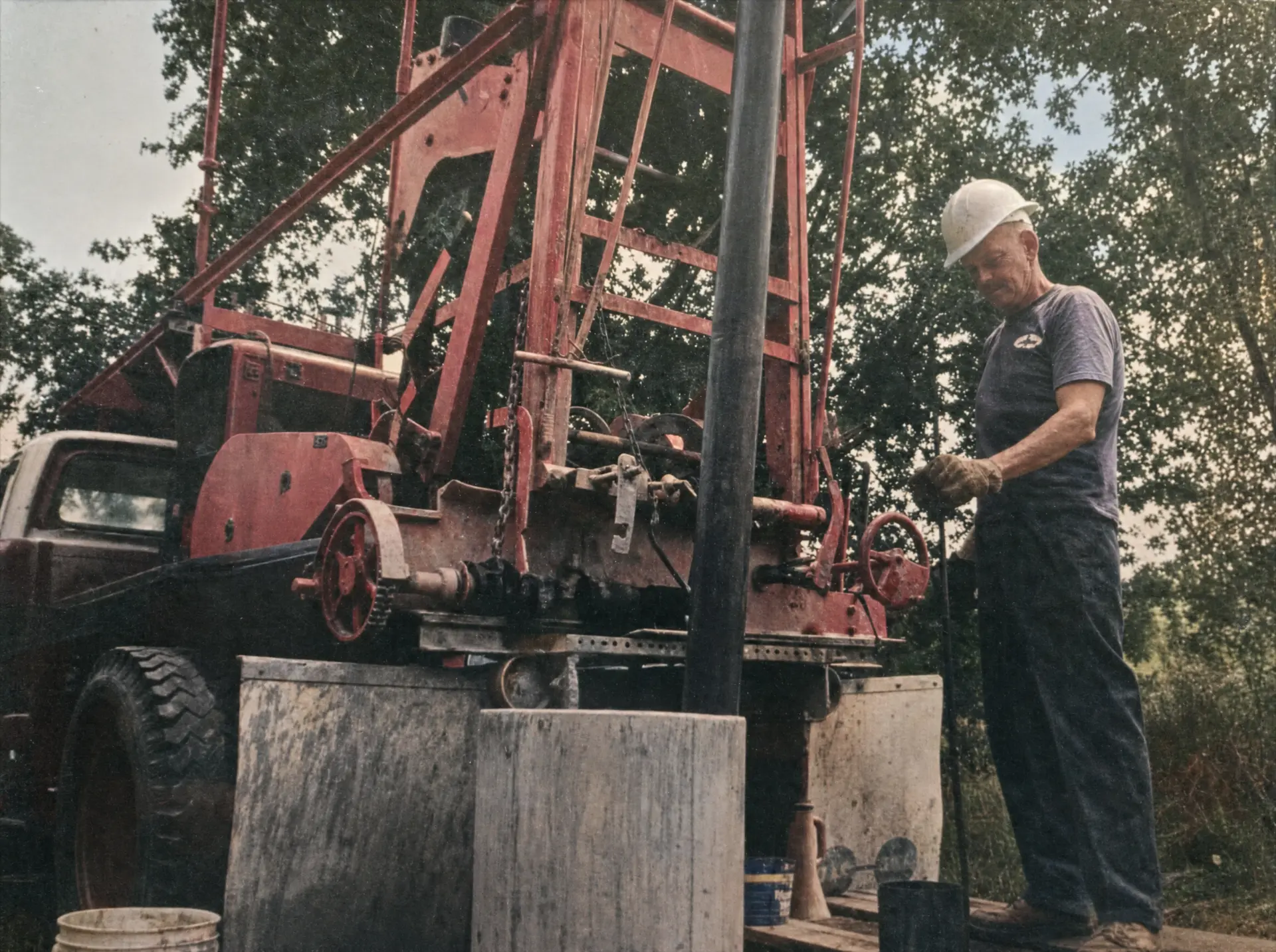 A Burgess family driller operating a vintage cable-tool rig mounted on an old red truck